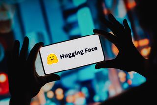 Hugging Face logo displayed on a smartphone held up in front of blurred background.