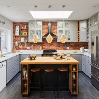 wooden island with stools, expose brick wall, grey cabinets and stainless steel fridge