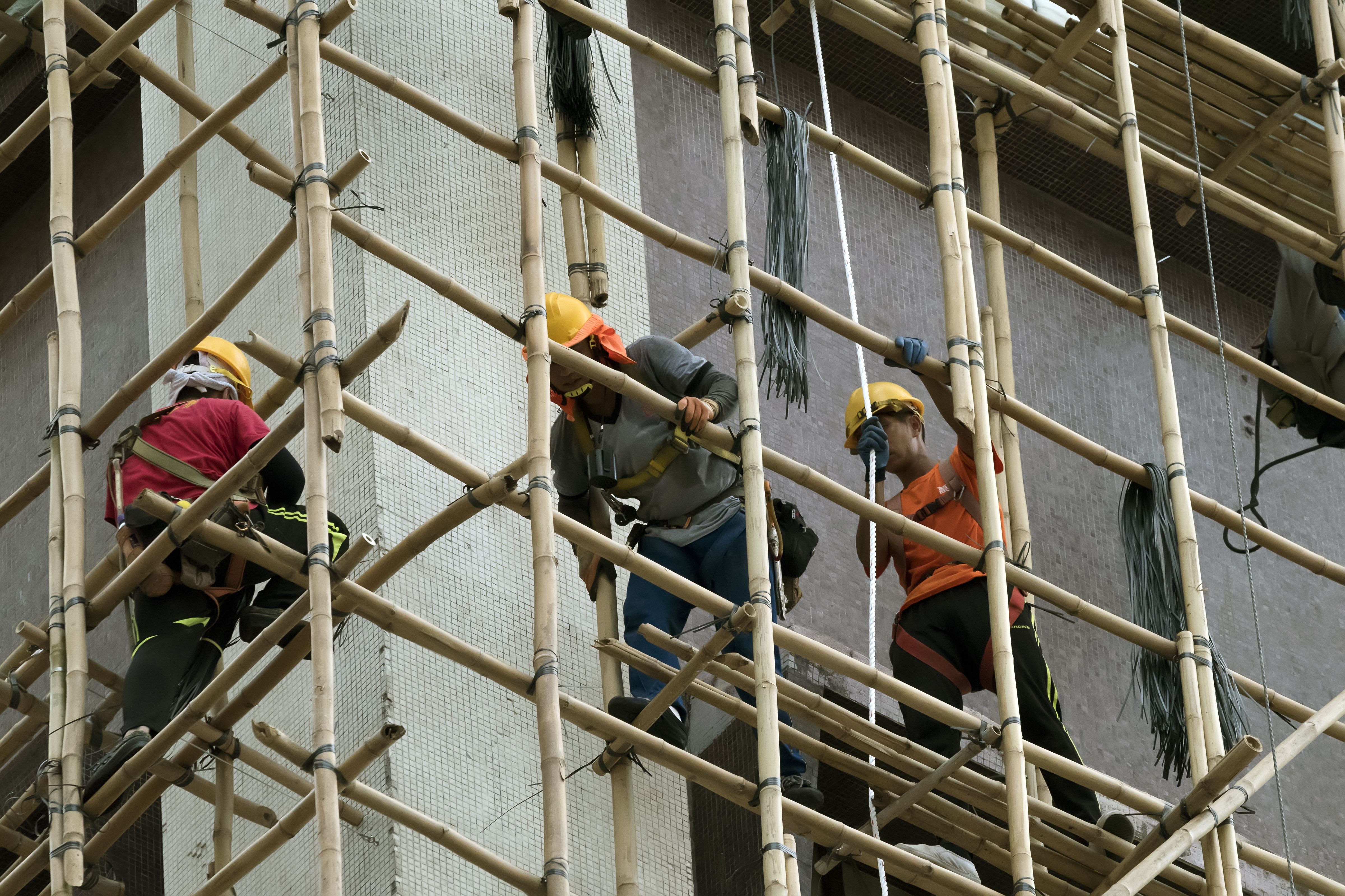 Chinese construction worker constructing bamboo scaffolding on the side of a building, Hong Kong, China