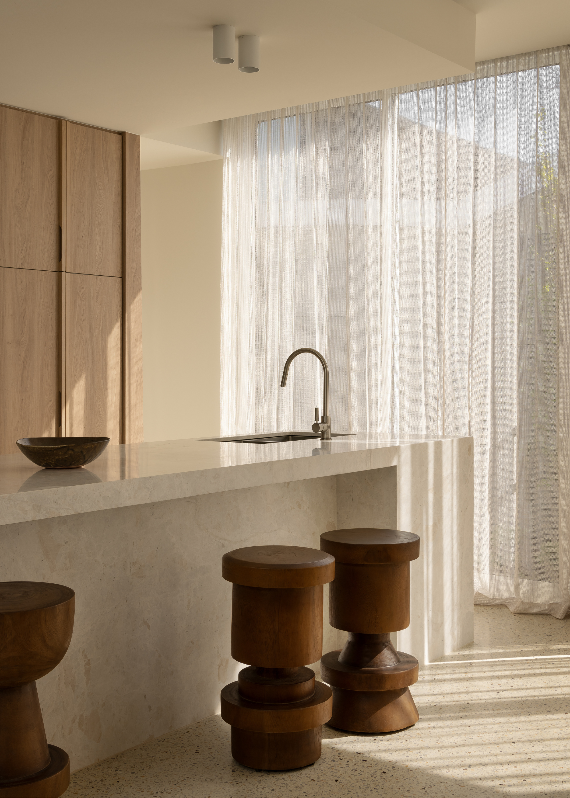 A minimalist kitchen with a trio of wood stools, a marble kitchen island and a bowl