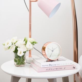 Rose gold lamp and alarm on top of bedside table with books and flowers