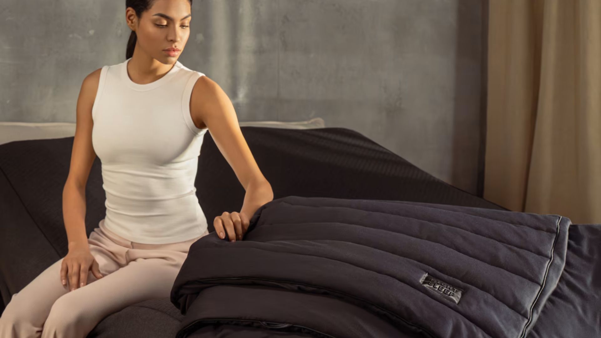 A woman sat on black elevated bed with Eight Sleep Pod 5 Ultra and thermo-blanket