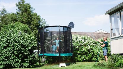 trampoline accessories kids jumping on a trampoline in the sunshine while their father sprays water at them from a hose