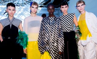 Models wear blac dress, sheer top with bra and yellow skirt, striped black and white dress, striped black and white top with black dress, and yellow top with white jacket and trousers
