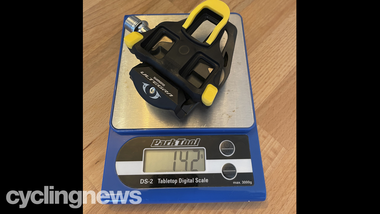 Shimano Ultegra pedals and a yellow cleat on a Park Tools scale, showing the weight of 142g