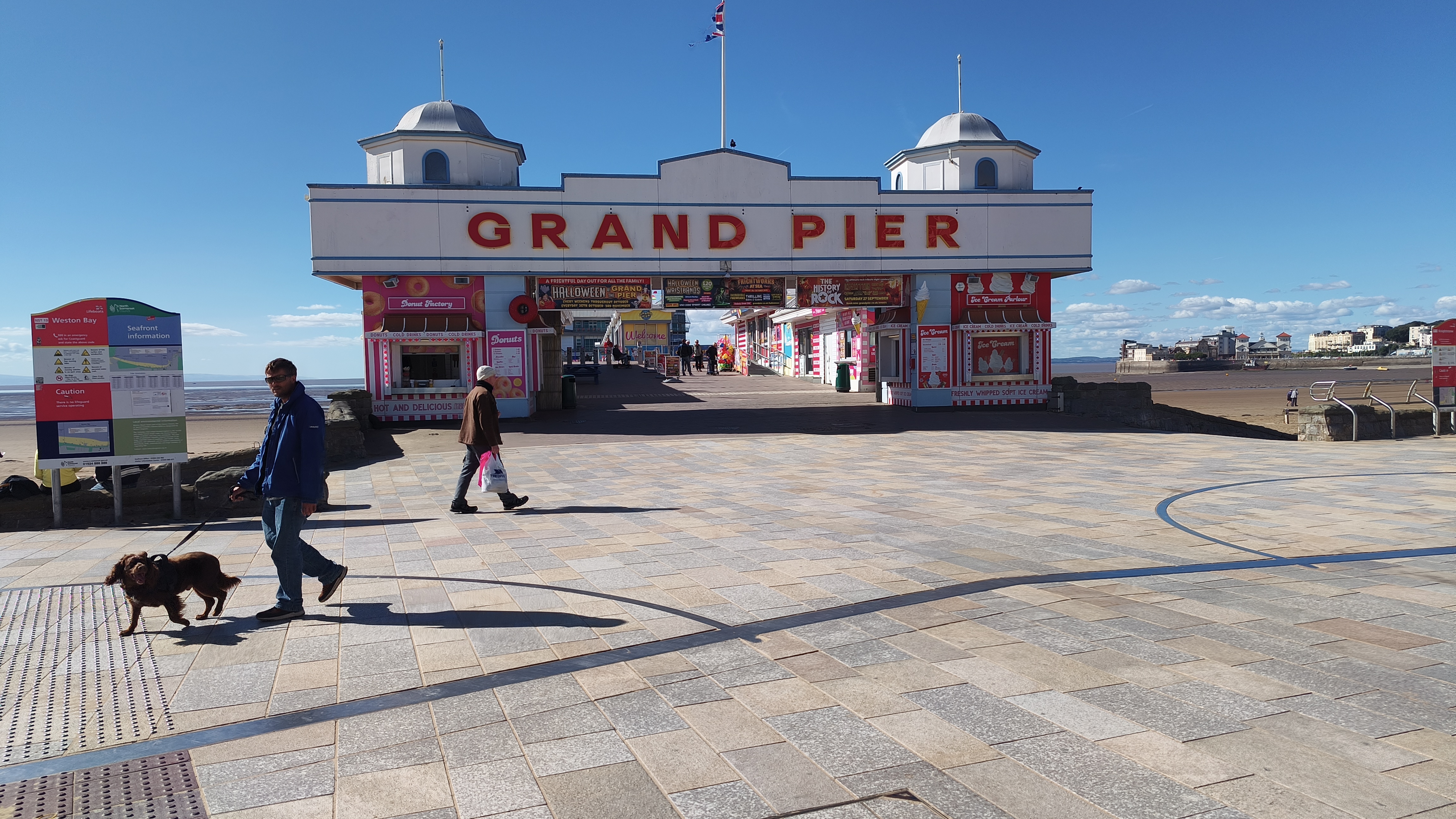 This image shows the main entrance to the Grand Pier amusement area, which has a large sign and various food stalls.