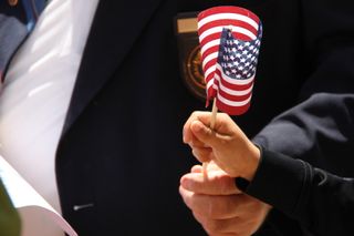 The hands of a veteran adult and a child hold a small American flag.