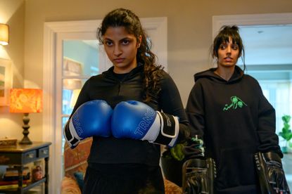 Priya Kansara does a martial arts pose in a green and gold dress against a black background