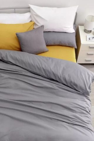 Plain grey bedding set on bed with mustard bottom sheet and pillow 