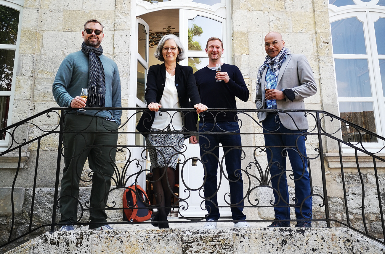 Four people standing on the terrace of a stone building