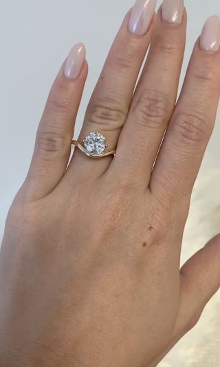 Woman wearing round-cut diamond engagement ring with curved gold setting.