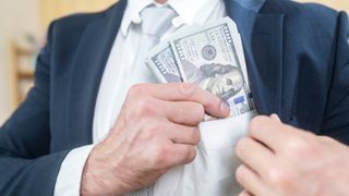 A businessman in a suit places cash into his pocket.