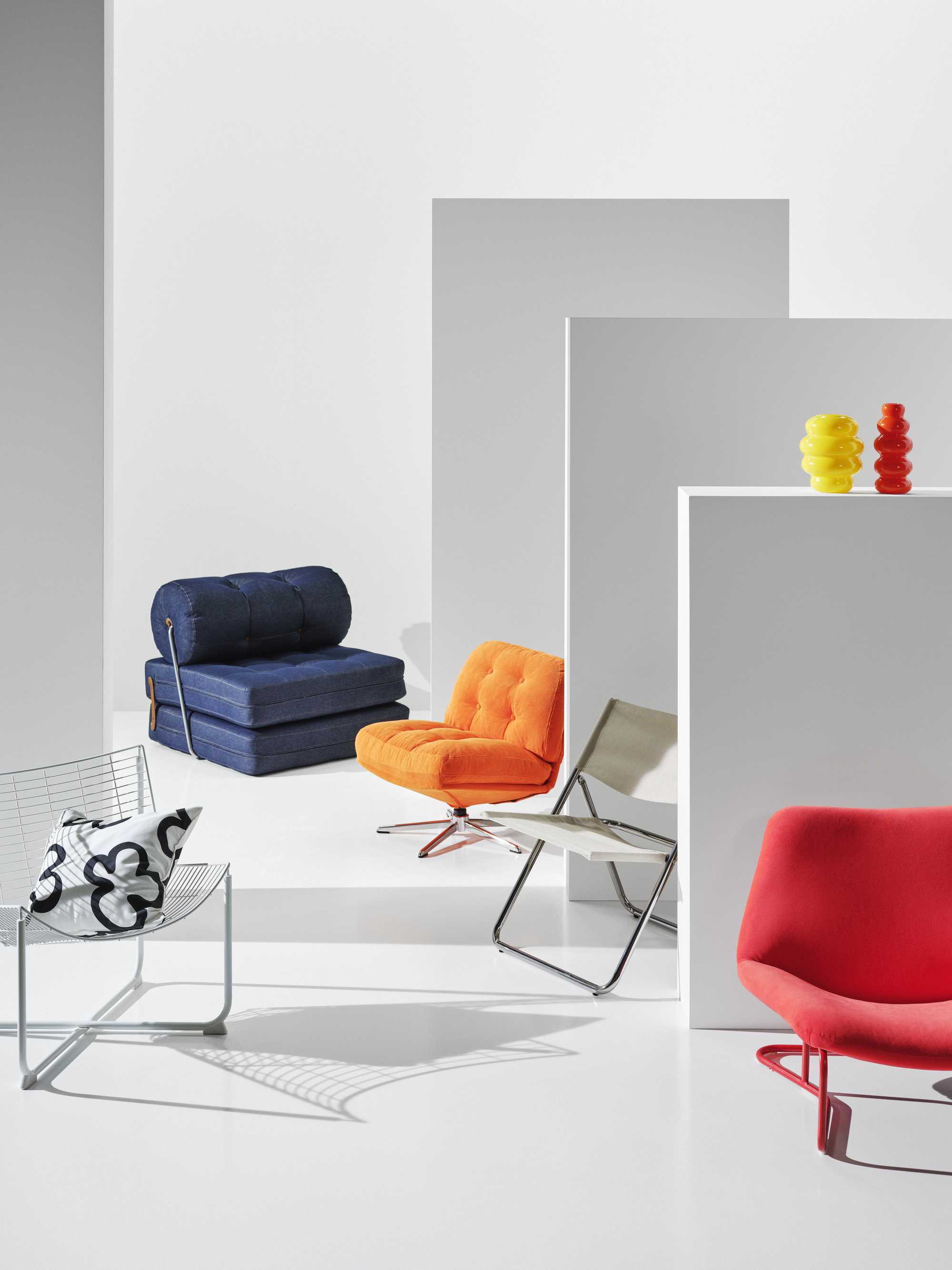 studio space with chairs from IKEA's Nytillverkad collection, including a denim fold-out sofa, wire chair, plush orange chair, folding chair, red chair and two vases