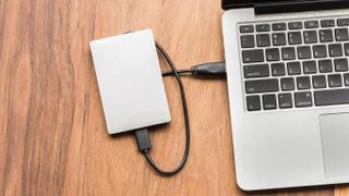 An image of an external hard drive with a brushed metal finish, plugged into a MacBook with a black USB cable