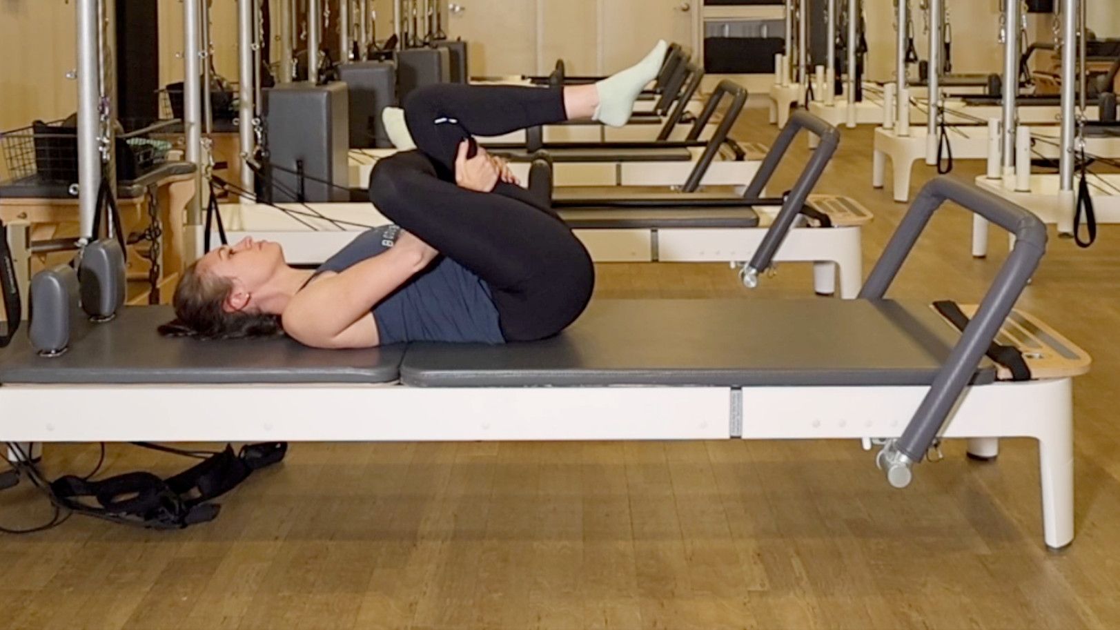 Woman demonstrating a Pilates exercise on the carriage of a Pilates reformer machine