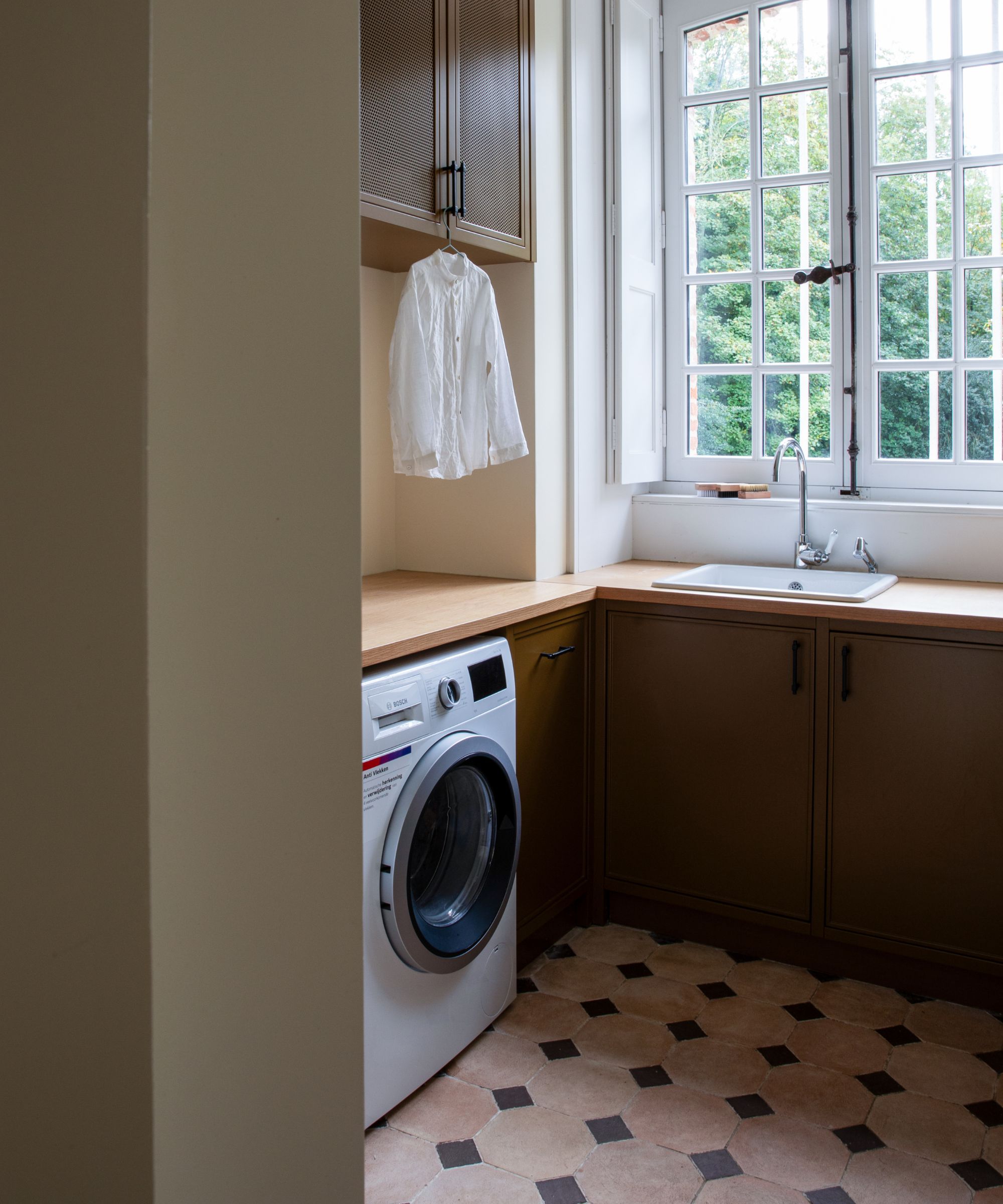 A small utility room with a washing machine beneath the counter, and a sink beside it. A shirt hangs from the cabinet handle above it.