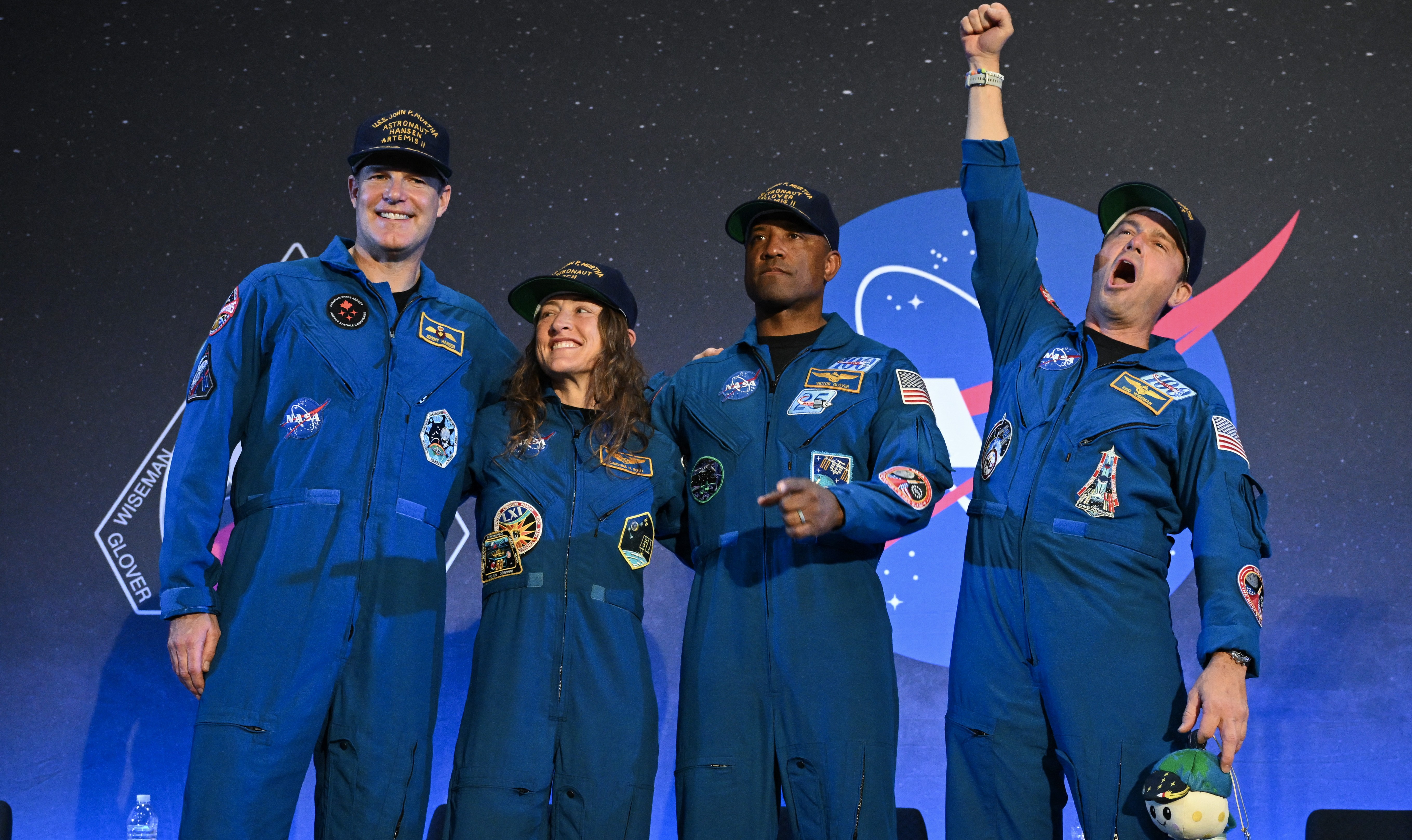 The Artemis II crew stand in front of the NASA logo.