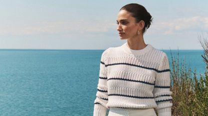 model wearing a striped White + Warren summer sweater standing in front of ocean