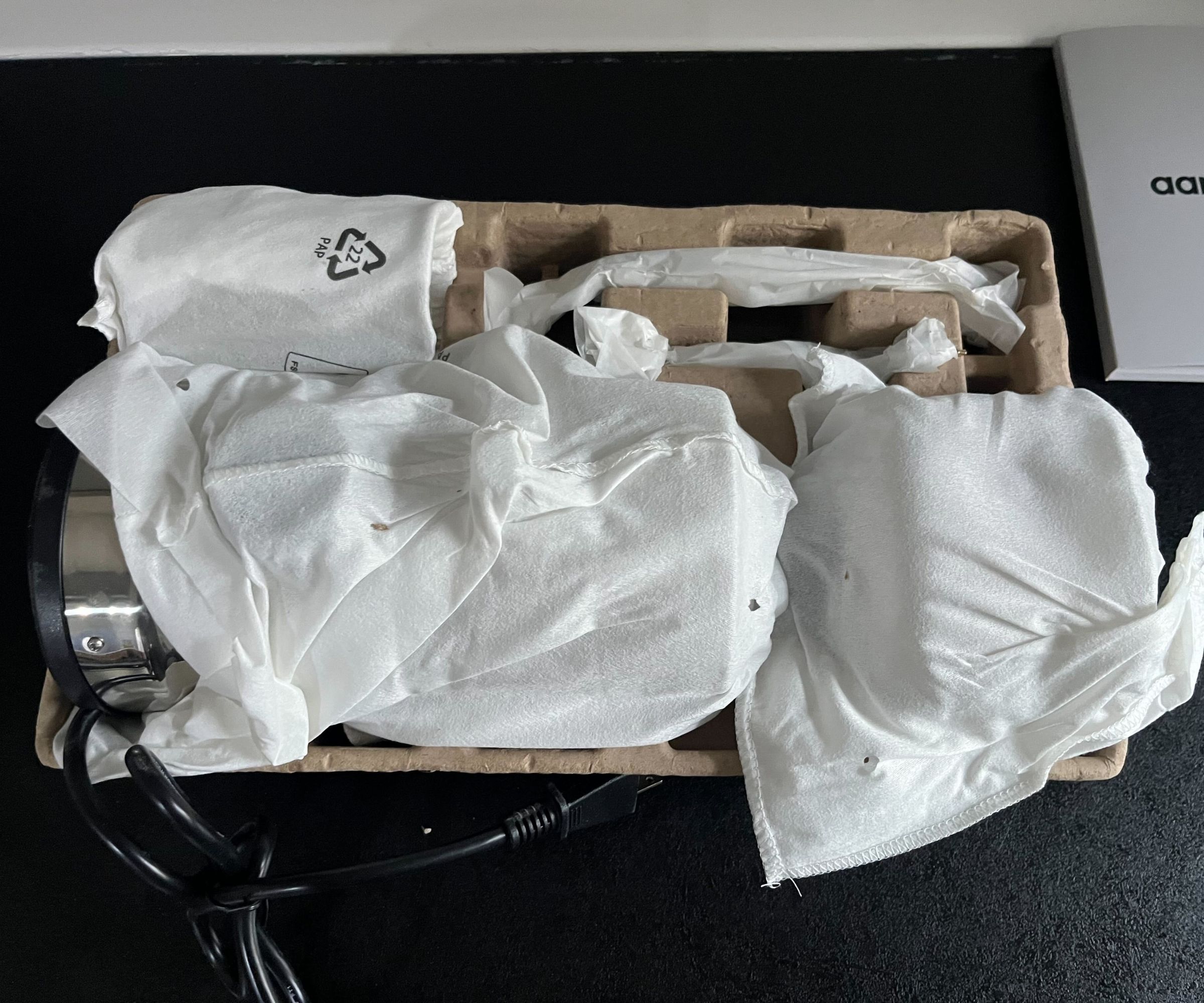 Cloth bag covered coffee grinder parts in a cardboard tray on a black counter