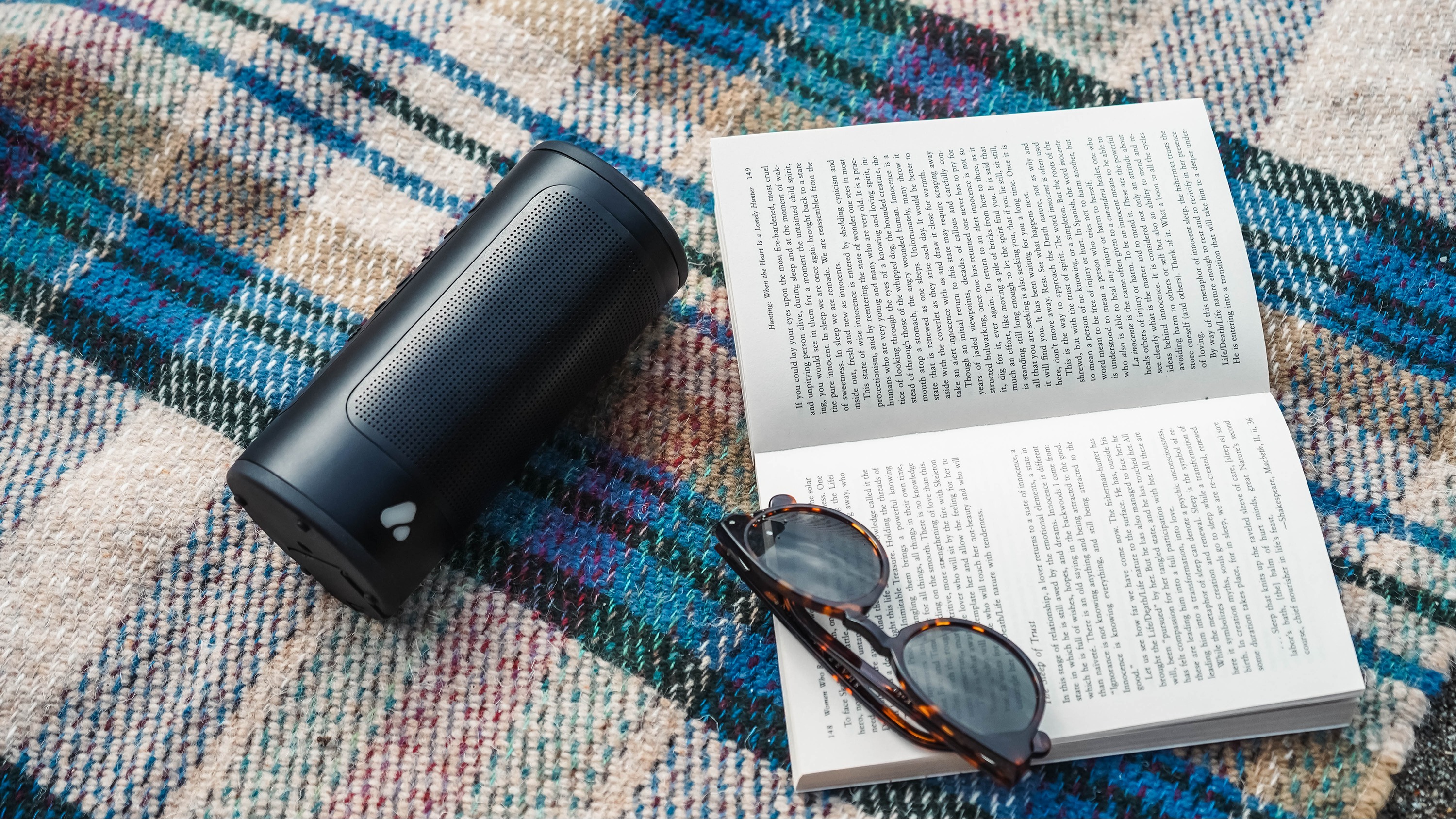 Poca Audio Pine Beat on a picnic rug next to a book