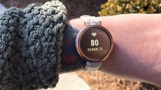 Garmin Lily smartwatch worn on a wrist outdoors with the heart rate measurement feature on the display.