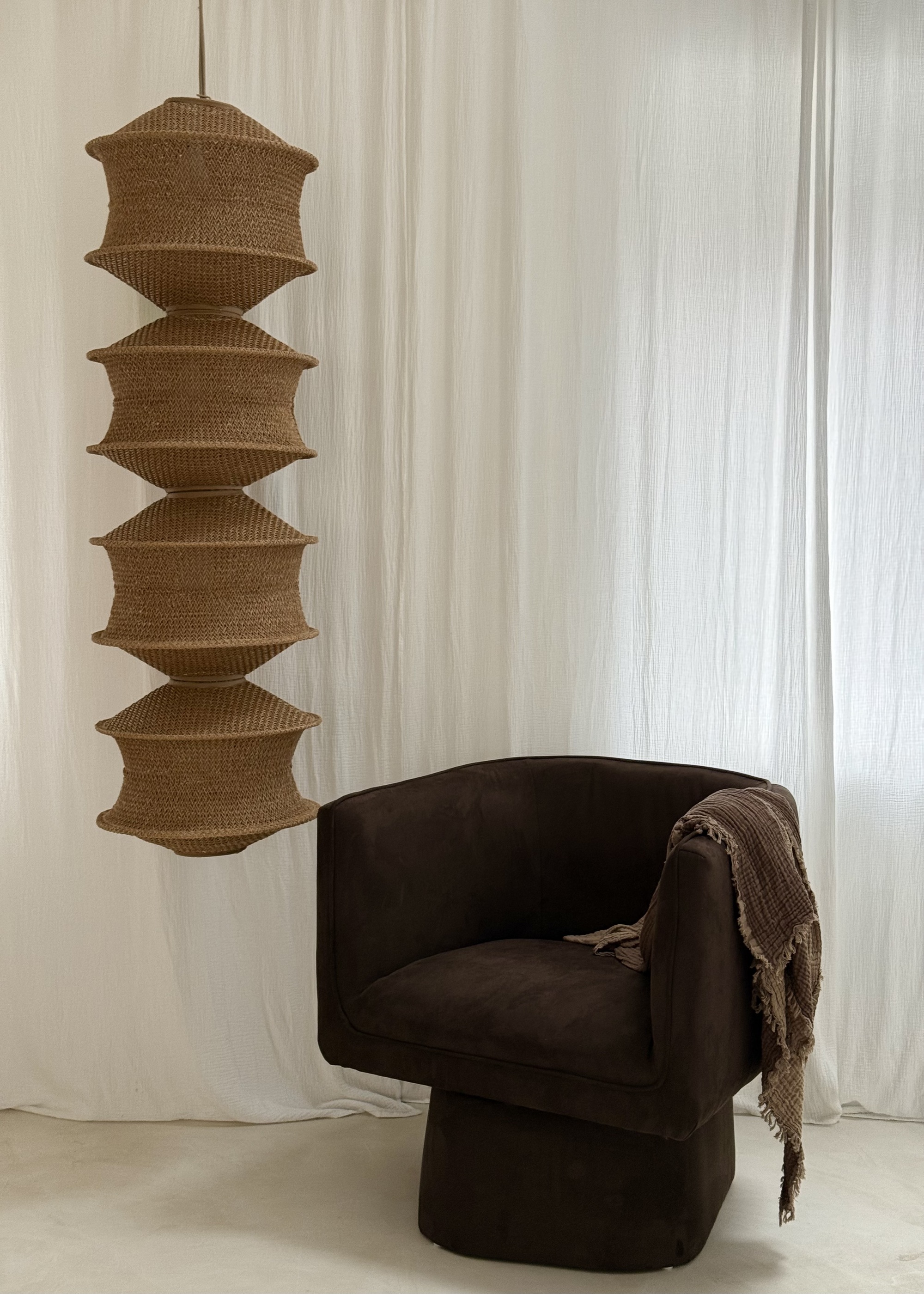 A neutral living room with a brown accent chair and a woven pendant lampshade suspended from the ceiling