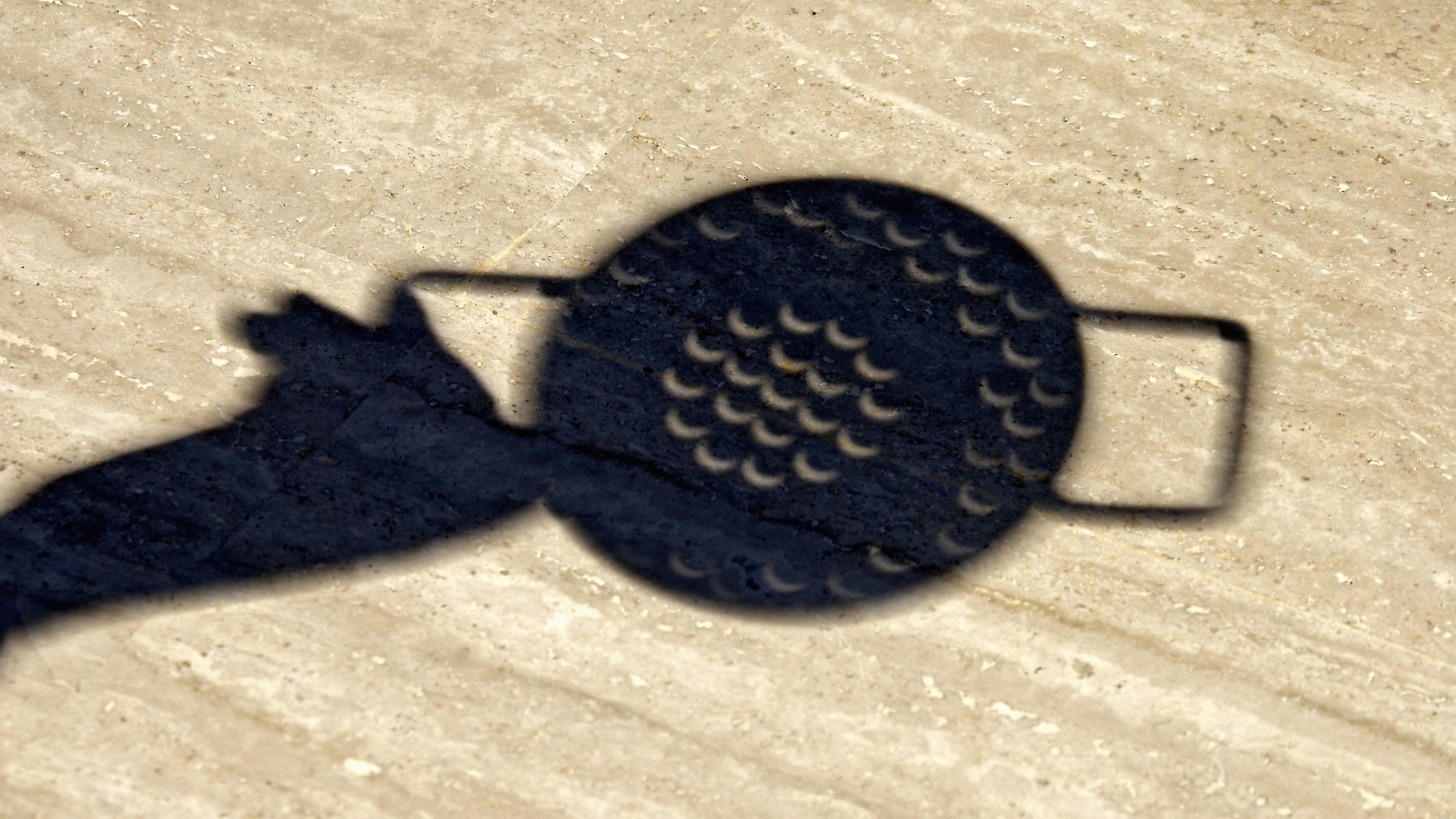 a shadow of a hand holding a colander and crescent shapes appearing through the holes.