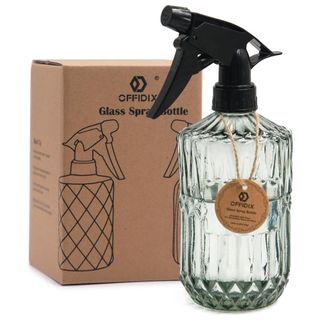 A cut glass plant mister with black spray lid filled with water next to brown cardboard packaging box