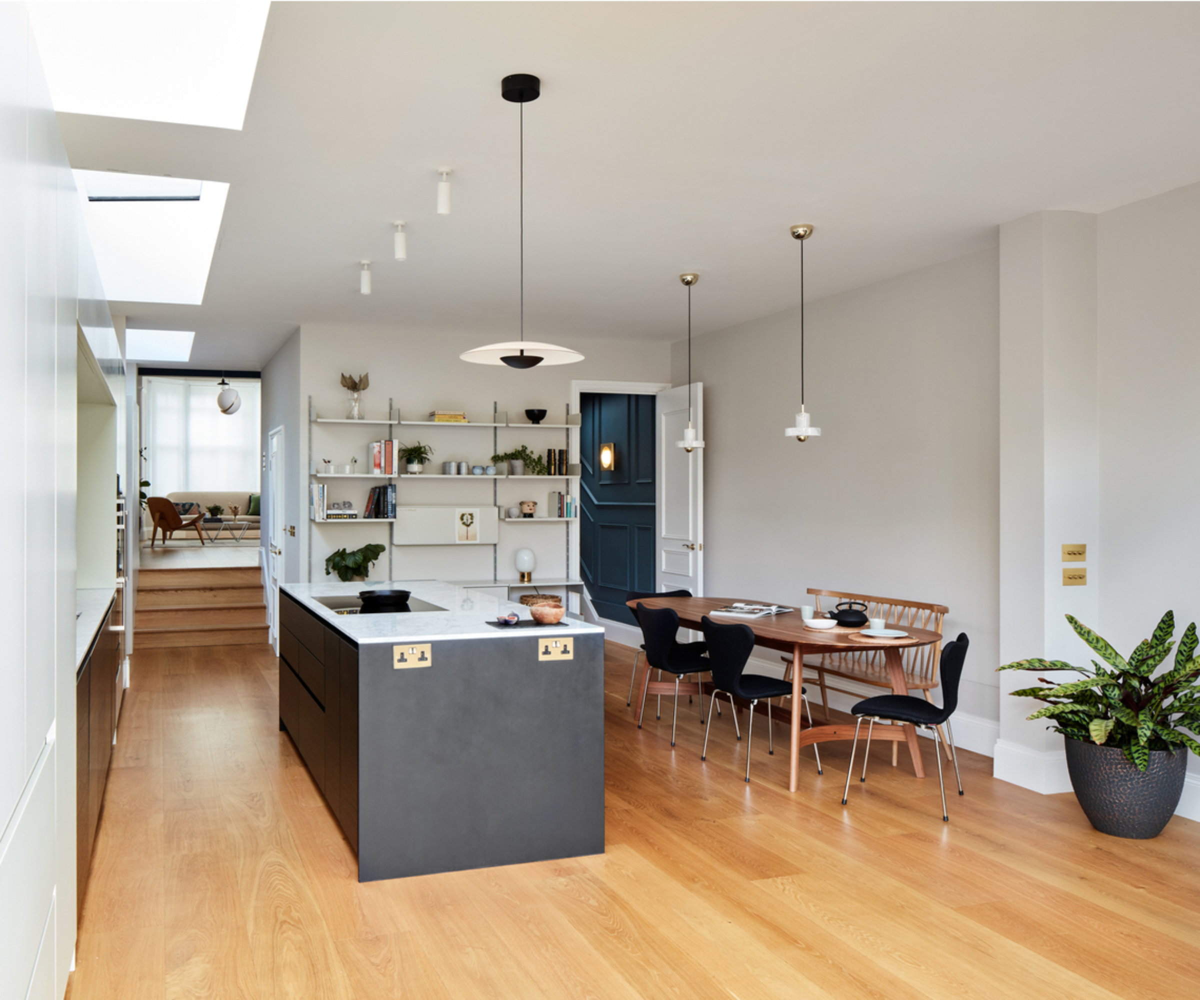 inside of wrap around kitchen extension with wooden floor, grey and white units, various pendant lights on ceiling and dining table and chairs