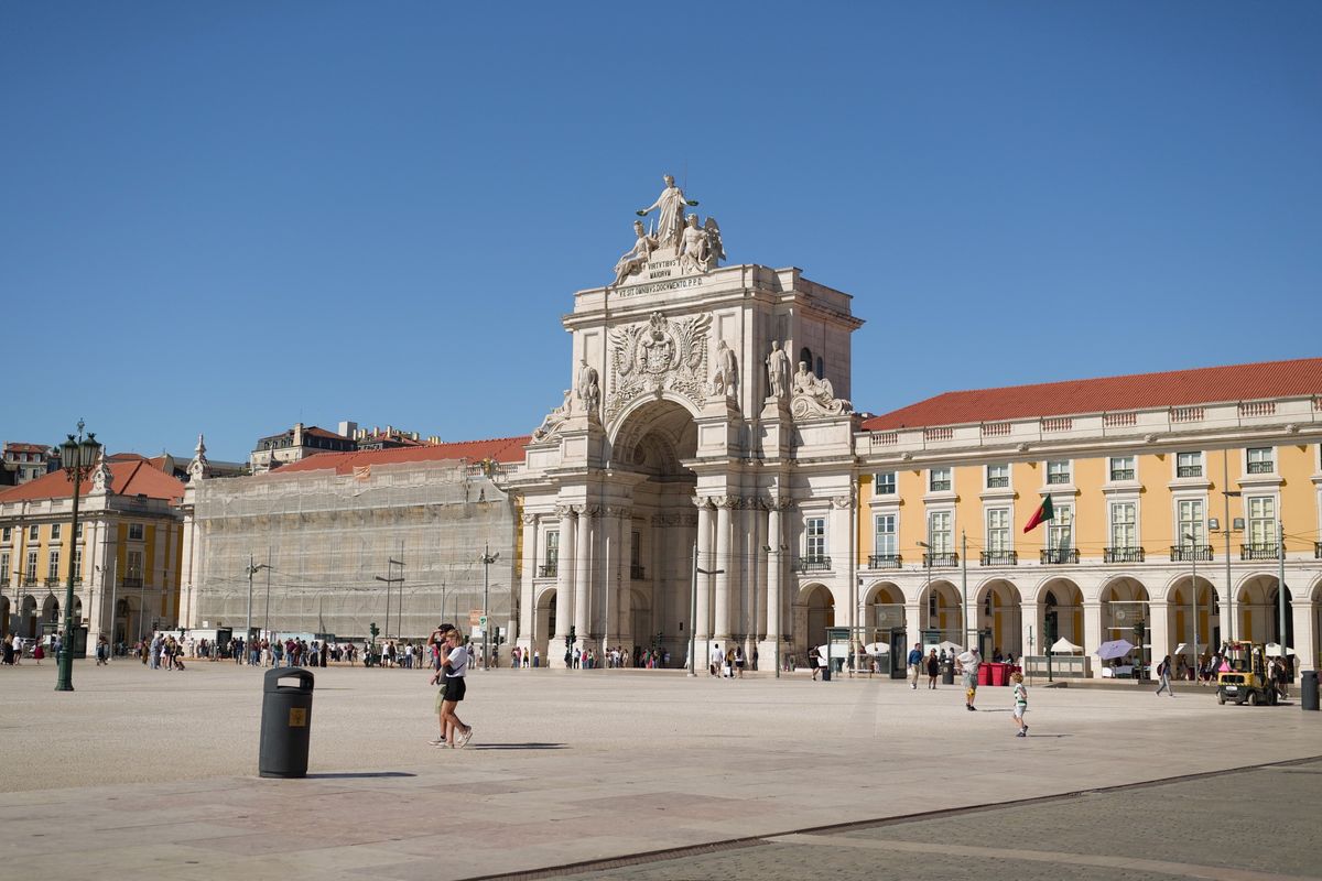 Arco da Rua Augusta and the surrounding yellow buildings of Pra&ccedil;a do Com&eacute;rcio under a clear blue sky.