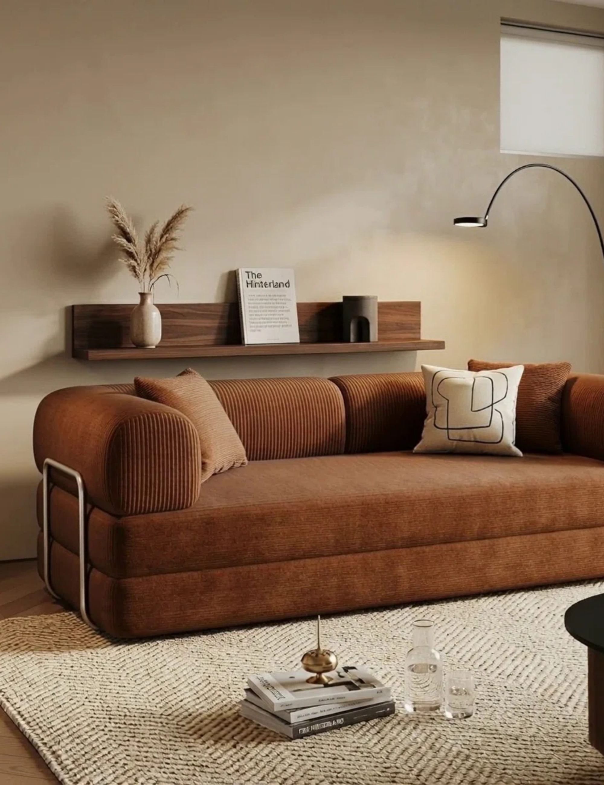 Terracotta 'boneless' sofa pictured in a neutral living room with an ivory herringbone-weave rug, a stack of coffee table books, and a modern wooden wall shelf.