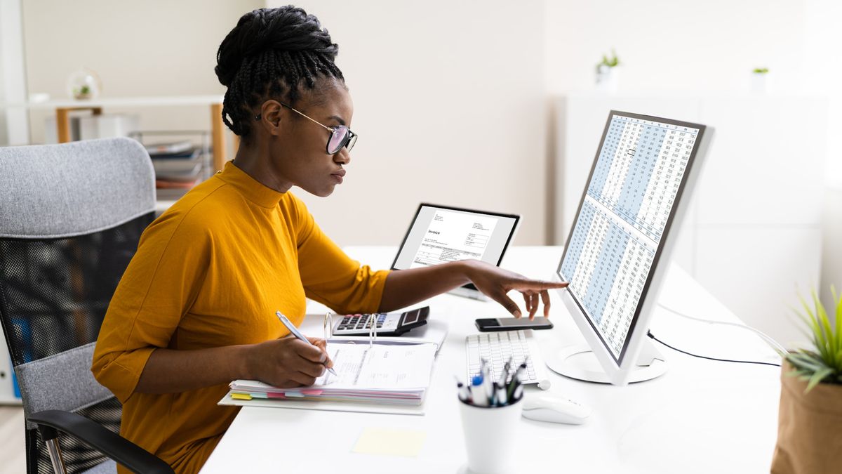 A person at a desktop computer working on spreadsheet tables.