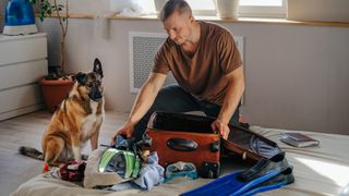 Man packing suitcase with dog watching