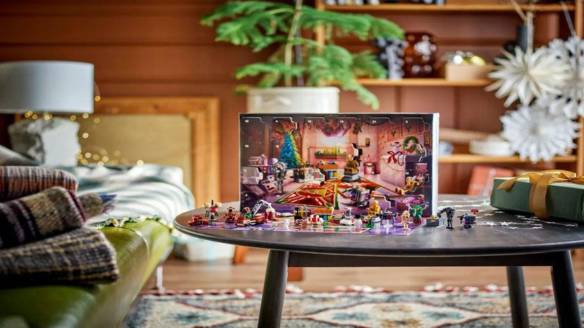 A festive workshop is displayed behind the various figures and mini builds included in the advent calendar, all displayed on a table in a living room.