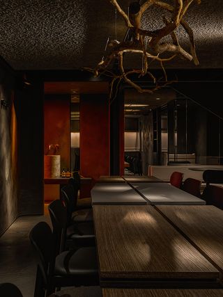 A dimly lit modern restaurant features wooden tables, metallic finishes, and a striking plant installation hanging over its main dining area.