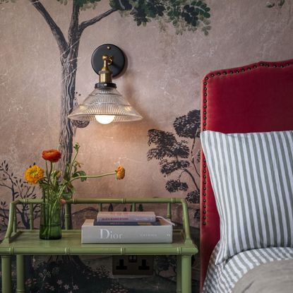 bedroom with bed, printed wallpaper, green bedside table and wall sconce