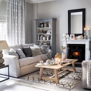 Light grey living room with grey patterned curtains, a grey shelving unit and an open fire