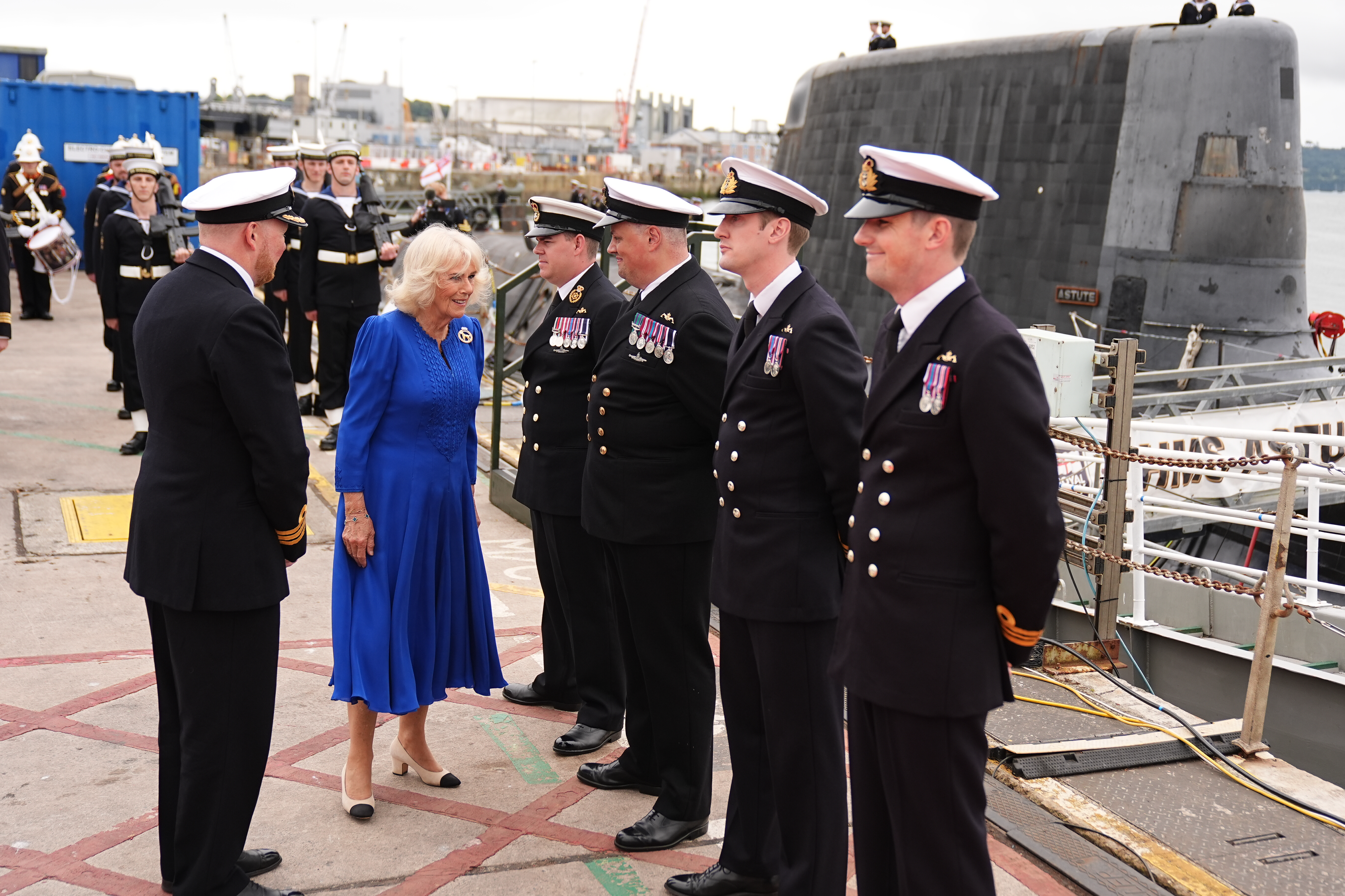 Queen Camilla wearing a blue dress talking to naval soldiers