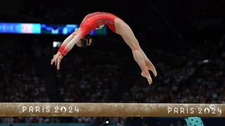 Yaqin Zhou of China pulls off an incredible backflip on the balance beam, in her red leotard, at the 2024 Olympic Games.