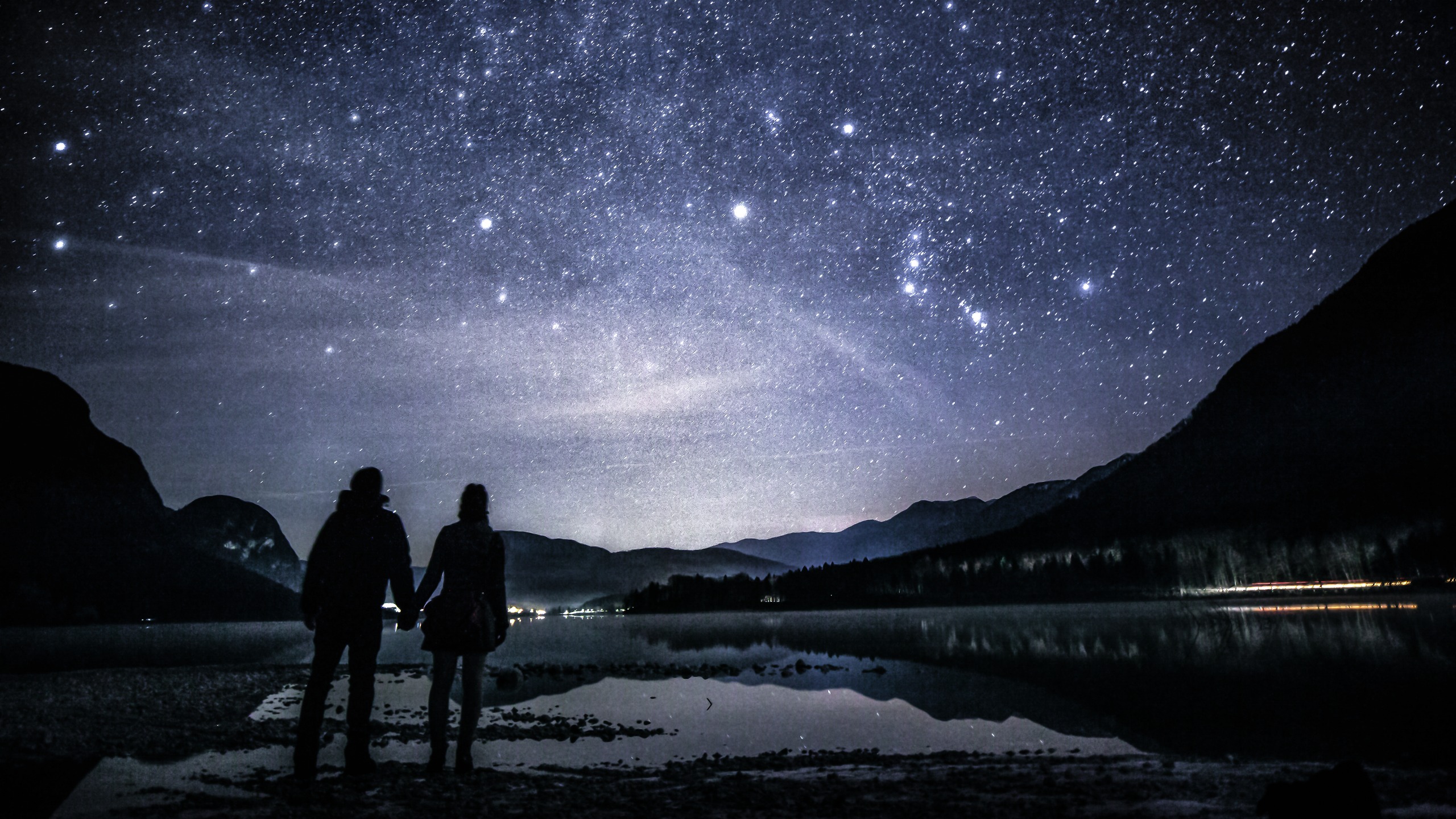 Couple holding hands by the lake and gazing at the stars. Orion belt is clearly visible