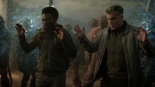 Two men holding up their hands in surrender. Behind them are zombies held back by a forcefield. L to R Babs Olusanmokun as Dr. MíBenga and Anson Mount as Capt. Pike in season 3, Episode 3 of Strange New Worlds streaming on Paramount+.