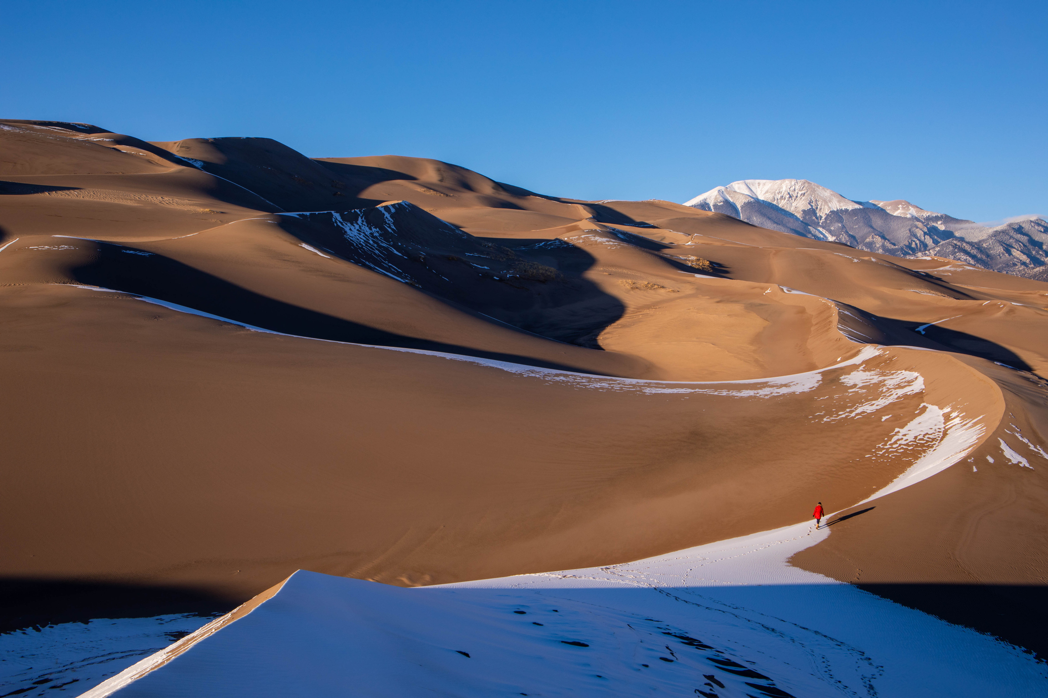 The sun hitting Great Sand Dunes National Park with a person walking and mountains in the background