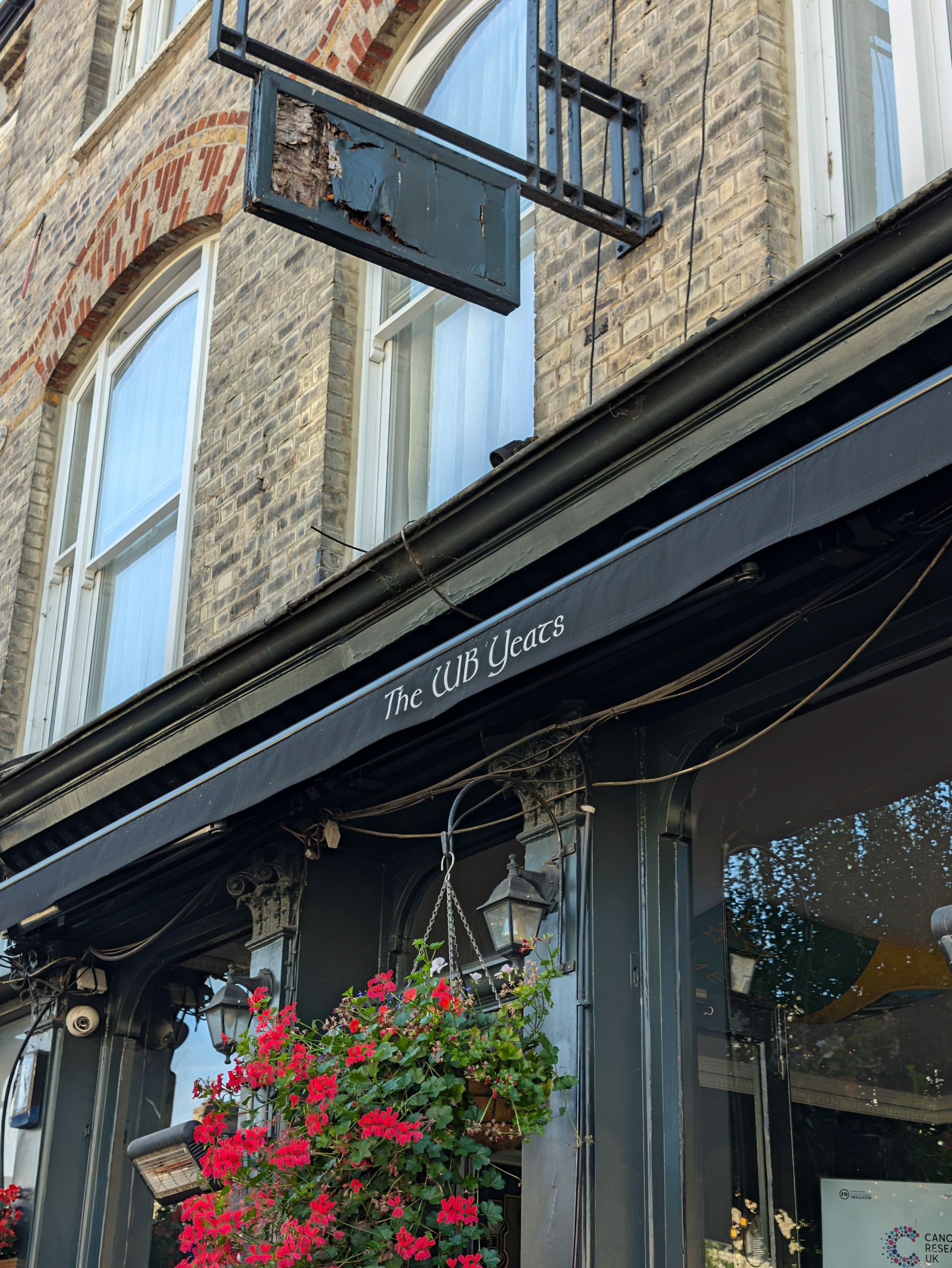 Exterior of The WB Yeats pub with black-painted frontage, hanging red flowers and brickwork above.