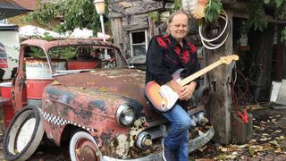 Walter Trout with guitar, leaning up against an abandoned truck