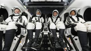 Four astronauts in white launch spacesuits giving thumbs' up signs.