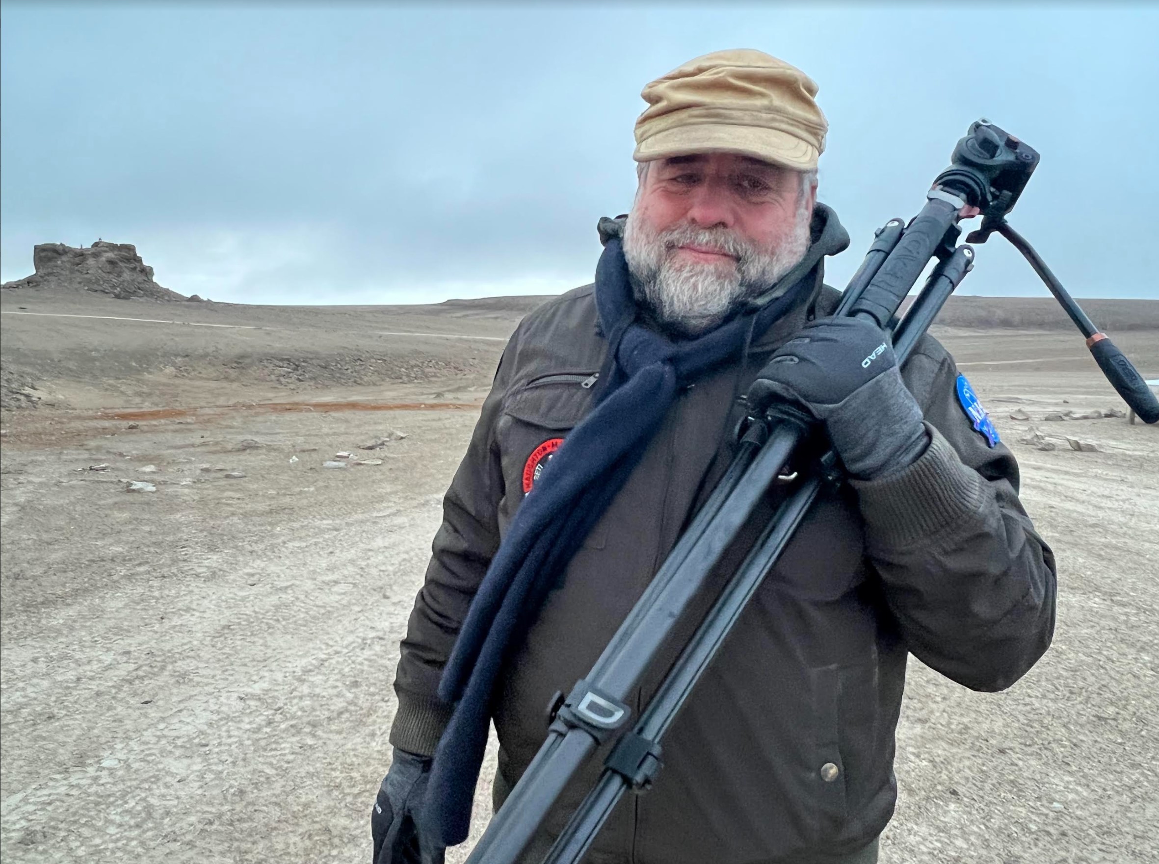 Rod Pyle stands in the Arctic holding a camera tripod.