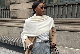 Nnenna Chem in a camel trench coat, white shawl, pinstriped trousers, and black handbag.