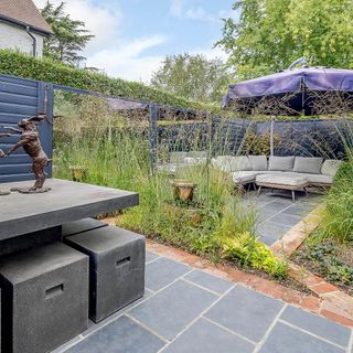 Garden area with grey tiles surrounding green plants and leading to an outside lounge area with grey couches