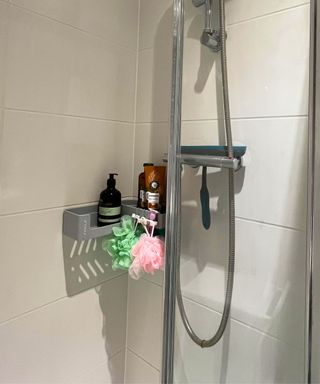 A white tiled small en suite bathroom shower cubicle with chrome fixtures, a gray corner shelf and bathroom soaps and shampoos