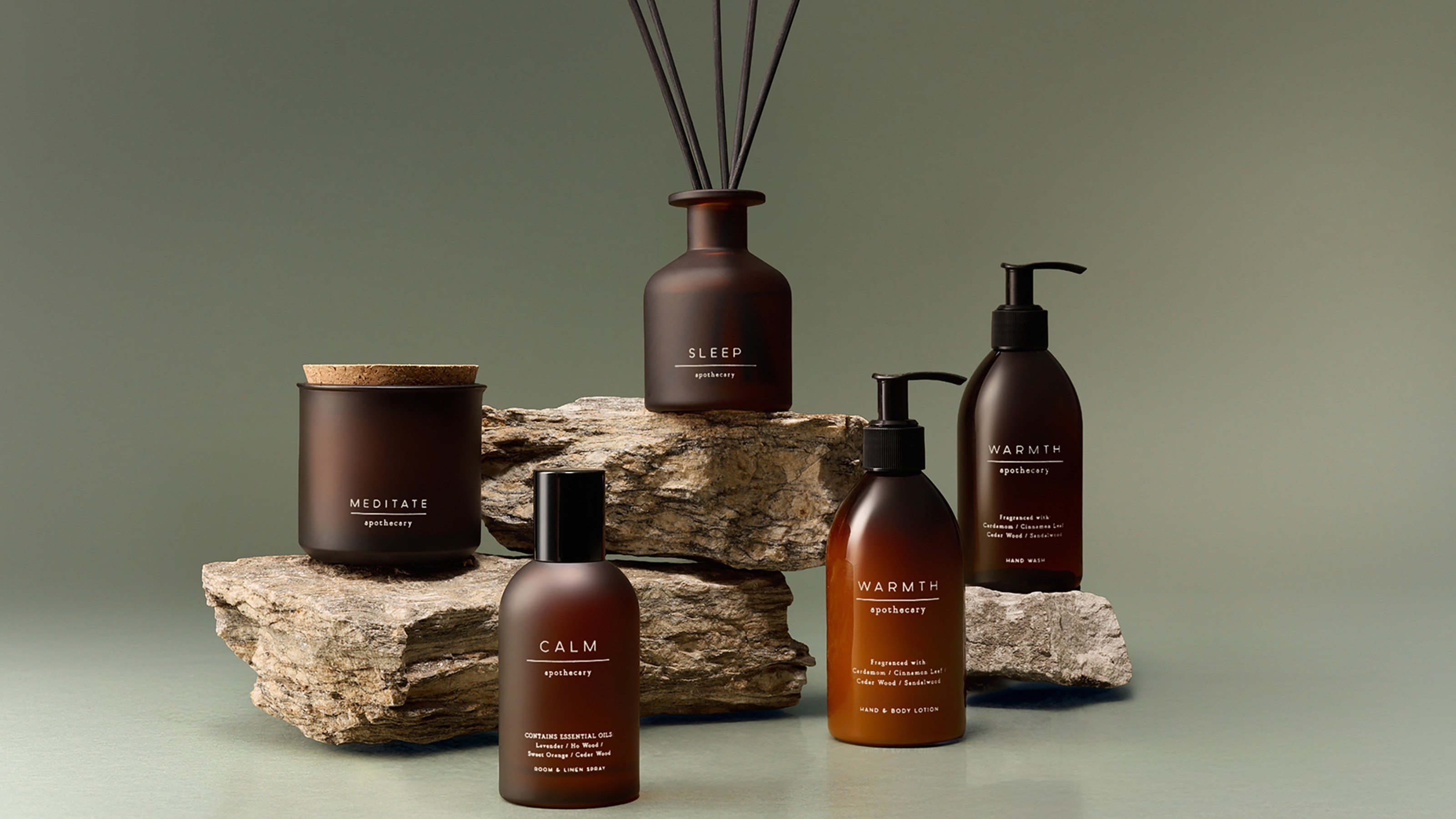 A candle, reed diffuser, room spray and ath body products from the M&amp;S Apothecary range displayed on stacked rocks